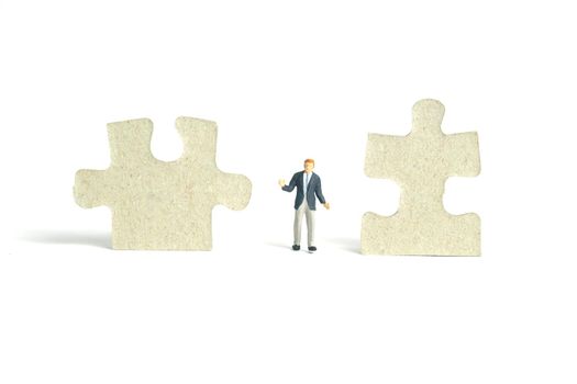 Miniature people toy figure photography. A shrugging businessman standing the middle of two puzzle jigsaw piece. Isolated on white background. Image photo