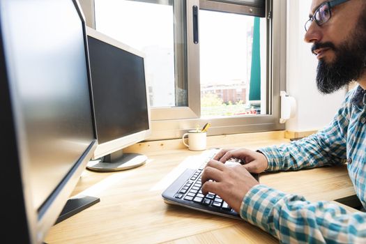 man typing on a keyboard in front of two computer screens, work from home concept