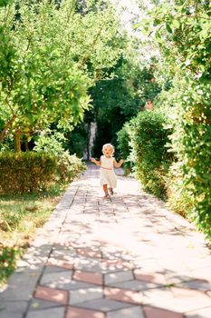 Little girl runs along the paving stones in a green park. High quality photo