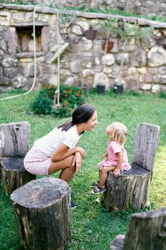 Little girl and her mother are sitting on stumps in the garden opposite each other. High quality photo