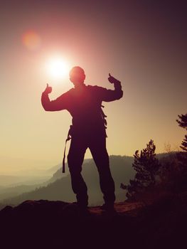 Happy man gesture of triumph. Funny hiker on the peak of sandstone rock in national park Saxony Switzerland watching into camera, the Sun behind head.