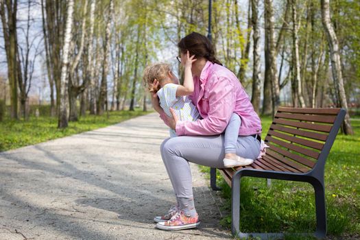 Exercise and play on a park bench. The caregiver swings the child up and down. A spring sunny day in a city park.
