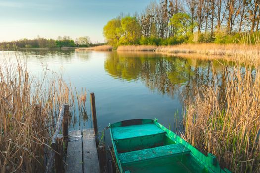 A boat moored at the pier in the reeds, calm lake and trees