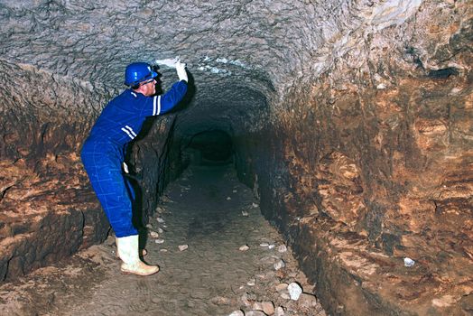 Worker in tunnel. Staff  in a protective suit check sediments in rocky wall, large underground tunnel sewer.