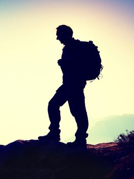 Tourist with sporty backpack stand on rocky view point and watching into deep misty valley bellow. Sunny spring daybreak in rocky mountains.