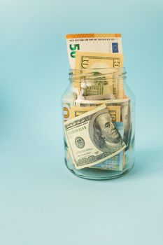 Money in international currency, including euro, dollar lies in a glass jar on a blue background. Place for an inscription