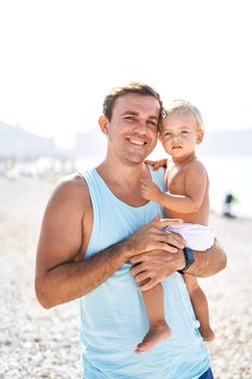 Smiling dad holding little daughter in his arms on the beach. Portrait. High quality photo