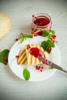 fried bread croutons for breakfast with redcurrant jam in a plate with berries on a wooden table.