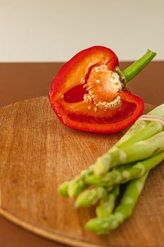 branches of fresh green asparagus on a wooden board, half of a red big pepper in the background. brown and light beige background. Basic trend concept with copy space