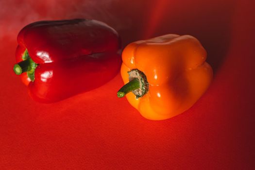 SWEET RED AND ORANGE PEPPERS ON A RED BACKGROUND.