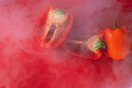 SWEET, fresh RED PEPPER ON A RED BACKGROUND, cut in half, thick smoke around. proper nutrition. fresh vegetables