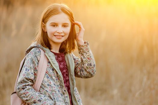 Preteen girl child looking at camera and smiling in amazing sunset light in the field. Beautiful portrait of pretty female kid