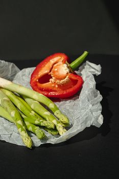 fresh green asparagus and half of red sweet, large pepper lie on white parchment on a dark gray background. proper nutrition. Lifestyle. place for text