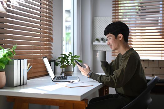 Side view asian man drinking coffee and reading online news on smart phone.