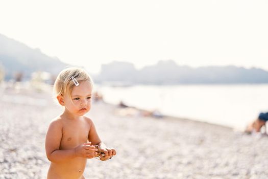 Little girl with sunglasses in her hands stands on the beach. High quality photo