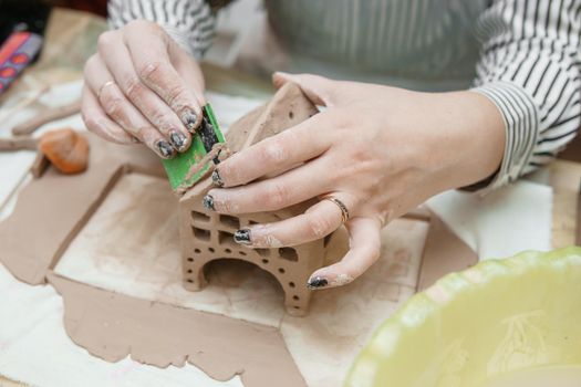 Women's hands knead clay, drawing elements of the product. Production of ceramic products at the master class on ceramics. Close-up.