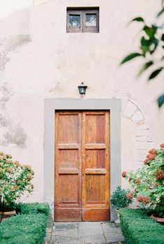 Wooden door in the stone wall of an old villa among green flowering bushes. High quality photo