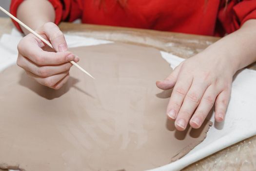 Women's hands knead clay, drawing elements of the product. Production of ceramic products at the master class on ceramics. Close-up. Making a candlestick in the form of a house. Christmas ceramic candle holder.