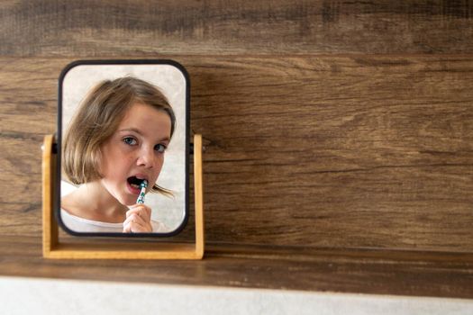 Oral hygiene, healthy teeth and care. Girl brushing teeth with toothbrush and looking in mirror in bathroom interior in the morning, closeup, empty space. High quality photo