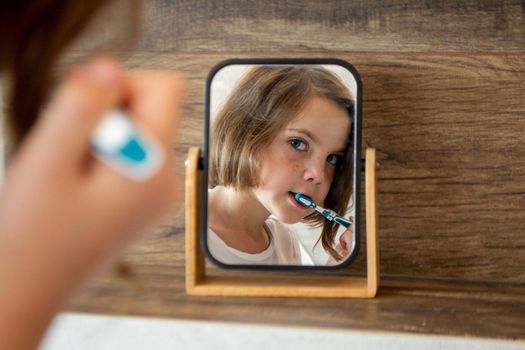 Oral hygiene, healthy teeth and care. Girl brushing teeth with toothbrush and looking in mirror in bathroom interior in the morning, closeup, empty space. High quality photo