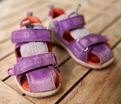 Top view of purple baby shoes on a table at home from above. Little girl footwear symbolizing new life, beginnings and pregnancy. Small stylish and fashionable sandals of a playful child on a desk.