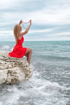 beautiful woman in a red dress on a white rock by the sea in summer