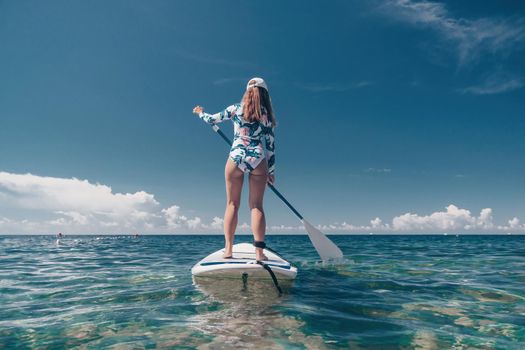 SUP Stand up paddle board. Young woman sailing on beautiful calm sea with crystal clear water. The concept of an summer holidays vacation travel, relax, active and healthy life in harmony with nature