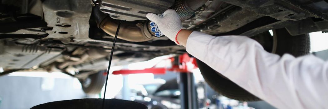 Close-up of mechanic man on car maintenance service change oil under transport. Garage with professional help and workers. Pit stop, fixing service concept