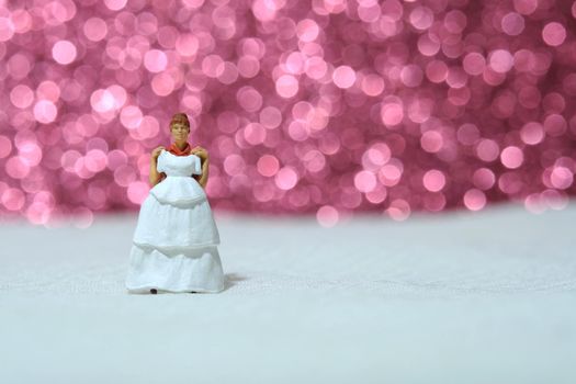 Women miniature people stand above white tile trying wedding dress with bokeh pink light background. Image photo