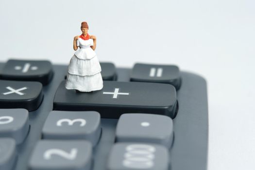 Wedding dress budget for bride, miniature people illustration concept. Woman standing above calculator. Image photo