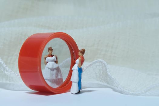 Women miniature people stand in front of mirror trying wedding dress. Image photo