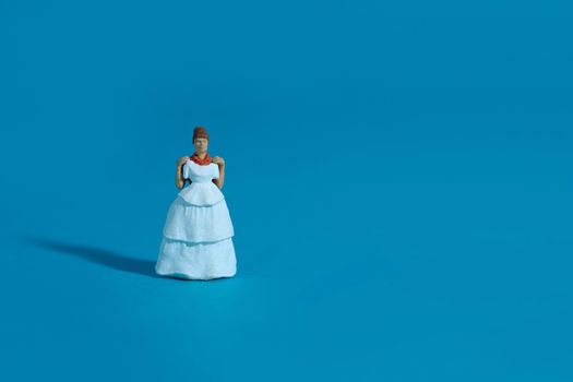 Women miniature people trying to choose wedding dress on blue background. Image photo