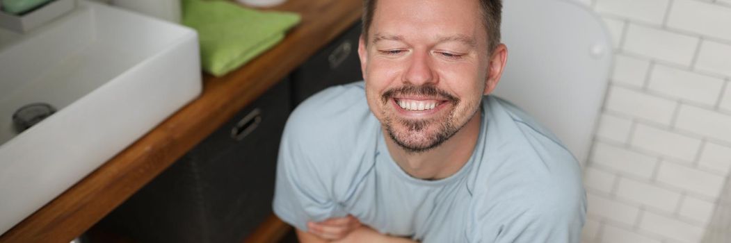 Portrait of man with happy facial expression after toilet, feel better after defecating. Man in bathroom after renovation. Wc, hygiene, nature call concept