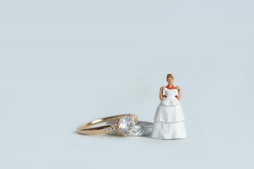 Women miniature people fitting wedding dress standing in front of couple ring, isolated white background. Image photo