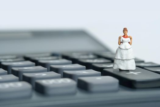 Wedding dress budget for bride, miniature people illustration concept. Woman standing above calculator. Image photo