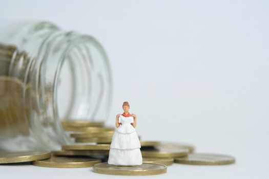 Wedding dress budget for bride, miniature people illustration concept. Woman standing above coin money jar. Image photo