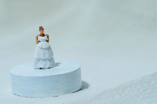 Women miniature people stand above white podium trying wedding dress. Image photo