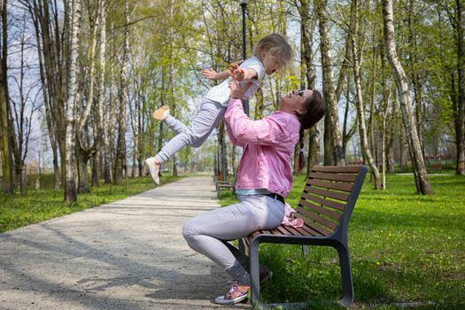 Joyful play with a child in a city park. Mother and daughter relax outdoors on a sunny day.