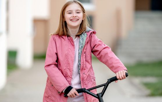 Smilling little girl rides a kick scooter on a street near home