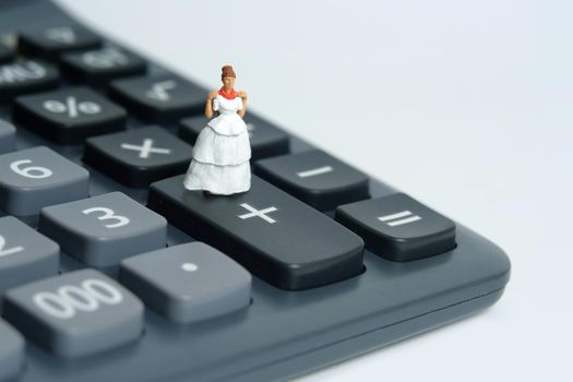 Wedding dress budget for bride, miniature people illustration concept. Woman standing above calculator. Image photo