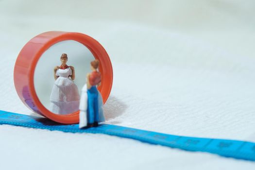 Women miniature people standing above measuring tape to fix her wedding dress. Image photo