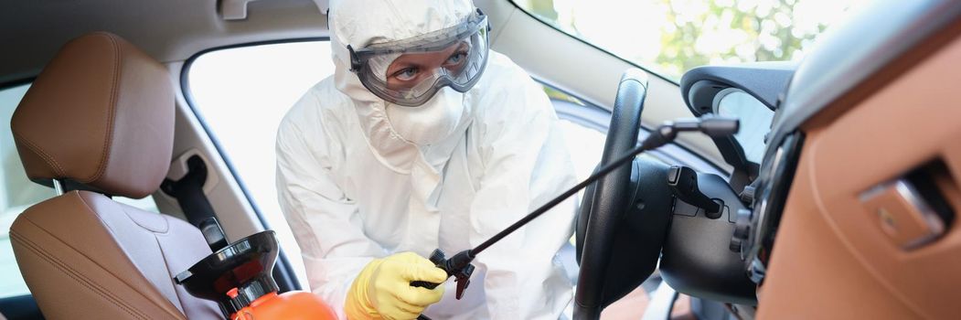 Portrait of hazmat female worker cleanse car interior with spray disinfectant. Disinfect auto upholstery from virus with equipment. Covid prevent concept