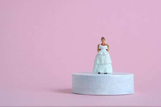 Women miniature people trying to choose wedding dress standing above platform pedestal on blue pink background. Image photo