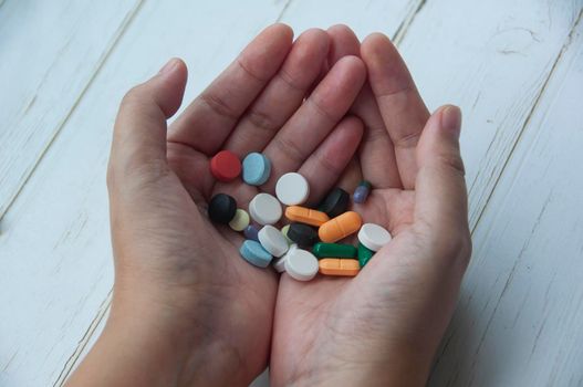 Female hand holding assorted pills isolated on wooden background. Copy space and Medical concept