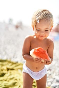 Little smiling girl with a piece of watermelon stands on the beach. High quality photo