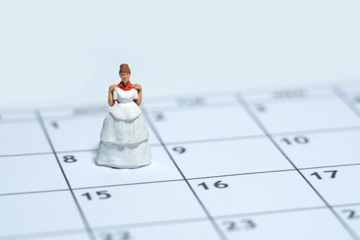 Woman miniature people stand above calendar while holding wedding dress, fitting day concept. Image photo