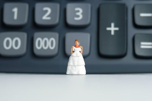 Wedding dress budget for bride, miniature people illustration concept. Woman standing above calculator. Image photo