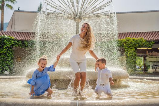Happy mother plays with her children in the street fountain.