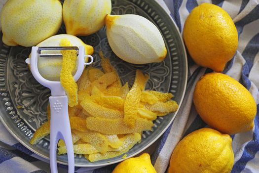 Lemon fruits and peeled strips for zest or making limoncello. Peeler, lemons and zest. Copy space, selected focus.