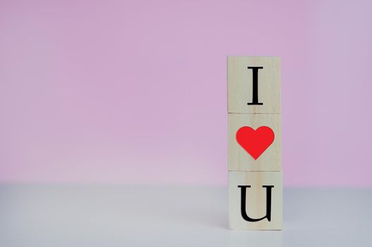 Wooden cubes with i love u symbol heart on the pink background and copy space.